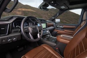 Luxury truck interior showcasing a modern dashboard with a large touchscreen, plush brown leather seating, and advanced driver assistance features, set against a scenic mountainous backdrop.