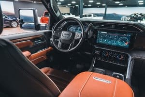 Interior view of a luxury vehicle showcasing leather seats, a modern dashboard, and advanced infotainment system, set in a well-lit showroom with various cars in the background.