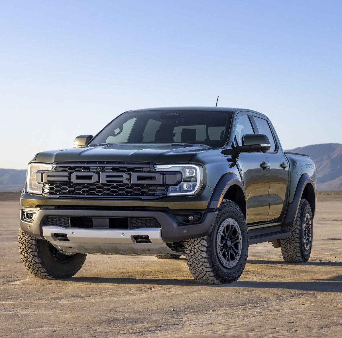 2023 Ford Raptor in black, showcasing rugged design and off-road capabilities, parked on a desert landscape under a clear sky. The truck features a prominent front grille with the 'FORD' logo and all-terrain tires, emphasizing its robust performance and adventure-ready styling.