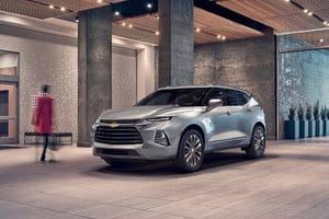 Silver Chevrolet Blazer parked in a modern urban lobby with a blurred figure walking in the background, showcasing its sleek design and upscale surroundings.