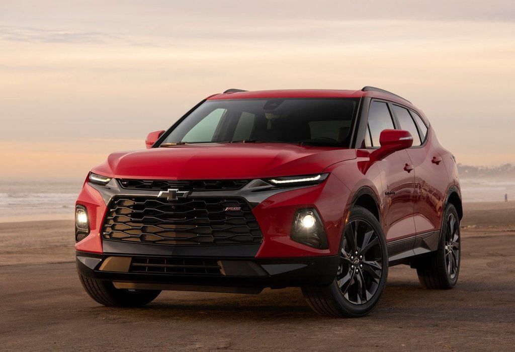 Red Chevrolet Blazer SUV parked on a scenic beach at sunset, showcasing its sleek design and modern features, including a large front grille and stylish headlights.