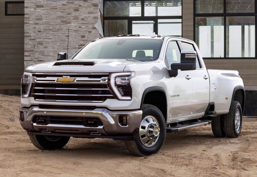 2023 Chevrolet Silverado heavy-duty truck parked on sandy terrain, showcasing a bold front grille, chrome accents, and robust design, ideal for towing and off-road capabilities.