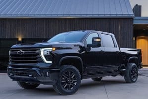Black Chevrolet Silverado 1500 pickup truck parked in front of a modern home with a sleek design and contemporary architecture, featuring aggressive styling and advanced LED headlights.