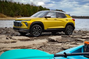 Yellow SUV parked on rocky shoreline with trees and calm water in the background, showcasing its modern design and off-road capabilities.