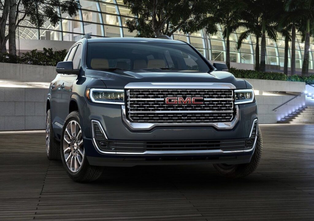 Front view of a gray GMC SUV showcasing its modern design and prominent grille with a red GMC logo, set against a contemporary architectural background. Ideal for highlighting a blend of style and functionality in vehicles.