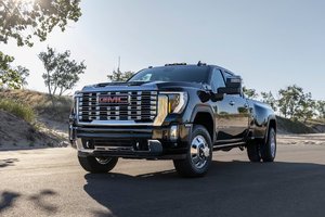 Black GMC truck parked on a scenic road with trees in the background, showcasing its bold design and chrome details on a sunny day.