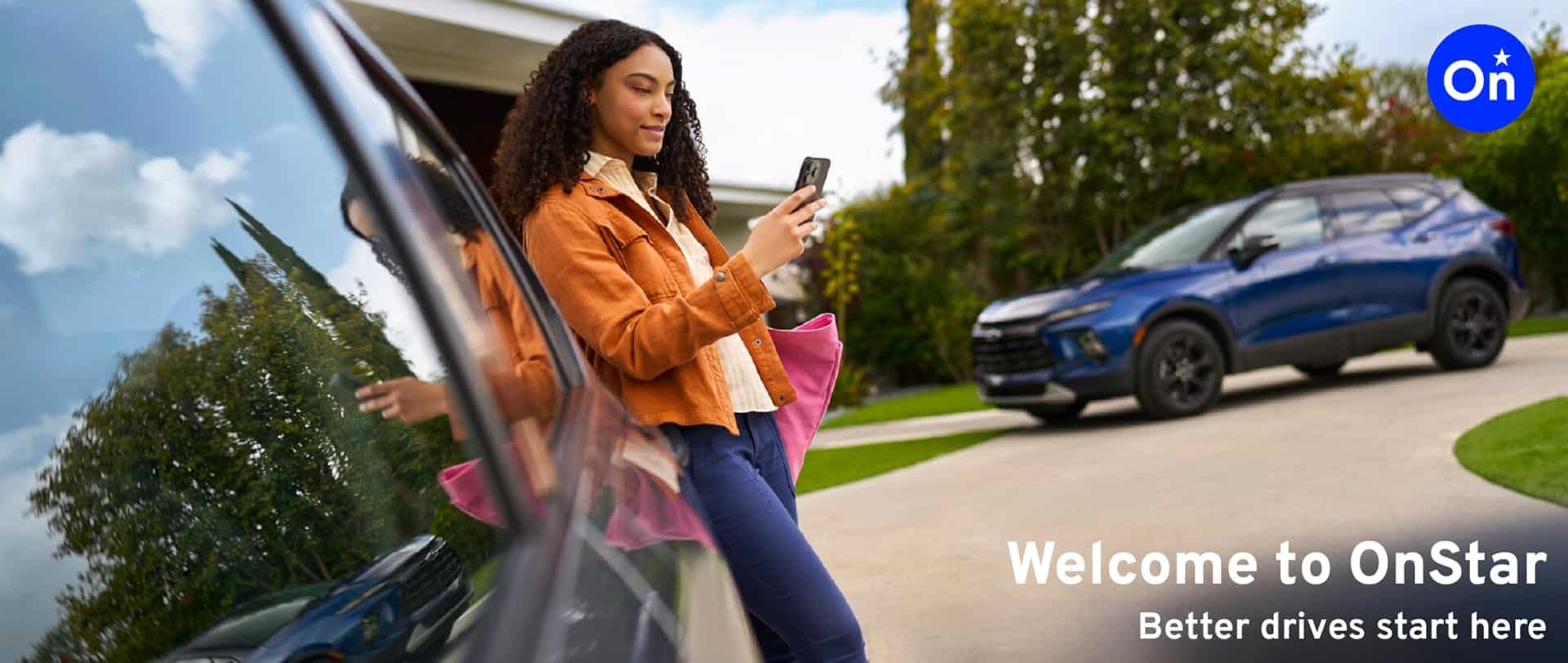 Woman using a smartphone while standing next to a black vehicle in a residential driveway, promoting OnStar services with a slogan "Better drives start here."