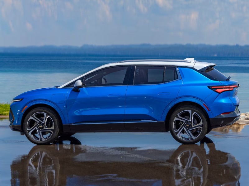 Blue electric SUV parked by a serene lake, showcasing its sleek design and modern features, with reflections on the water surface and a clear sky in the background.