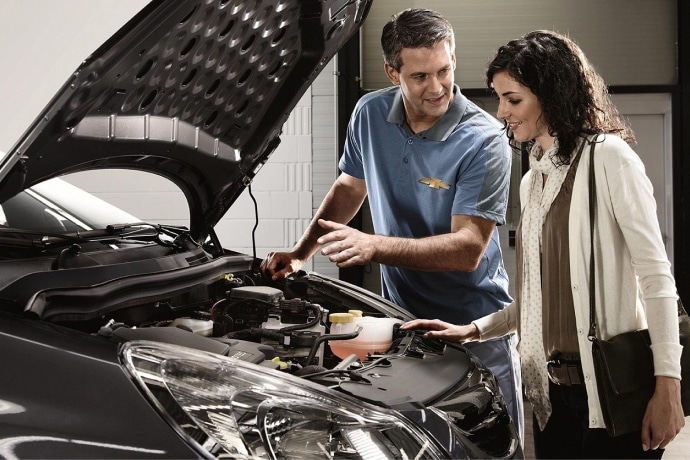 Mechanic explaining car engine components to a woman in a service center, highlighting customer service in automotive maintenance.