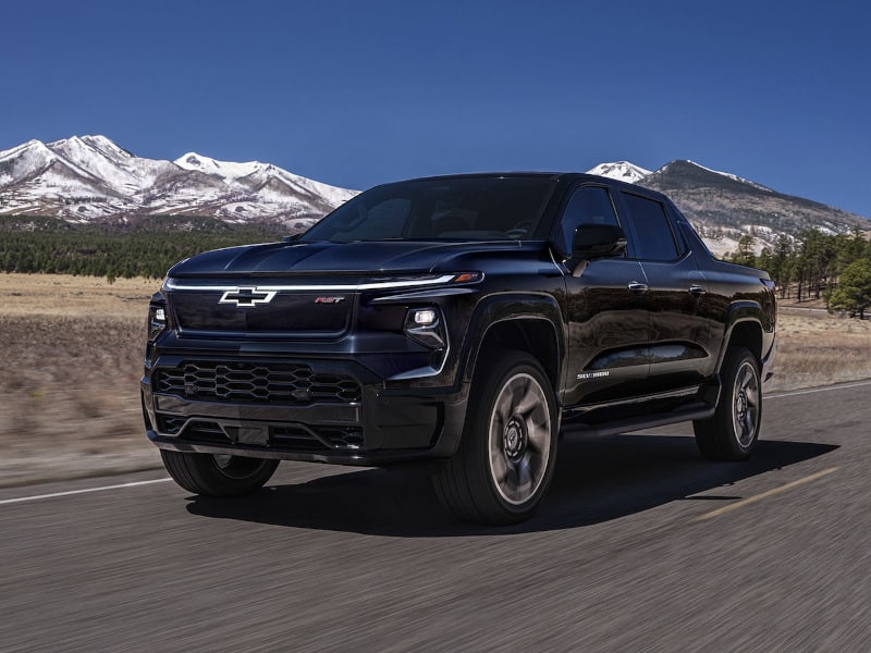 Black Chevrolet electric pickup truck driving on a scenic road with mountains in the background. The image showcases the truck's modern design and rugged capabilities, highlighting its performance in outdoor environments.