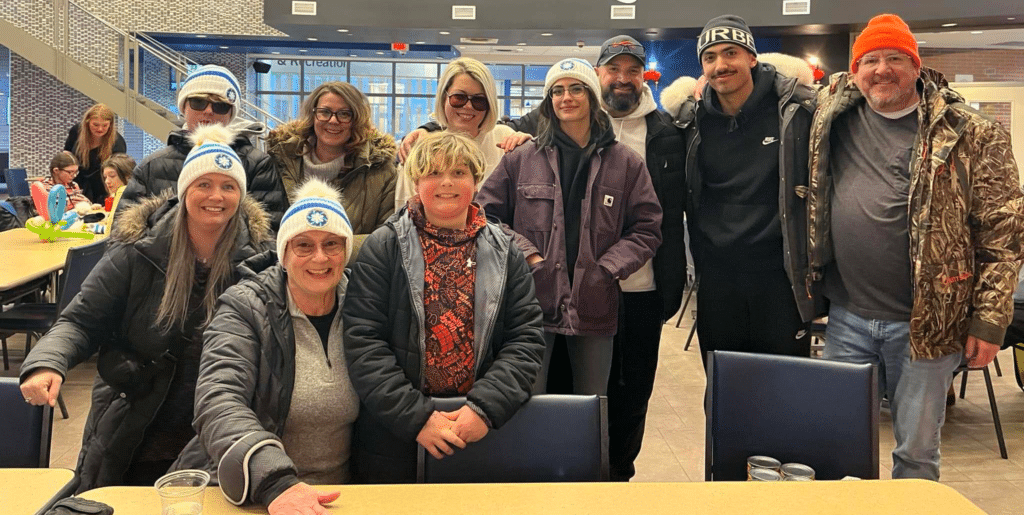 Group of smiling people in winter attire gathers in a cafe, enjoying a social gathering.